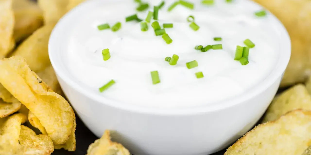 Schüssel mit cremiger Sour Cream, garniert mit Schnittlauch, umgeben von knusprigen Kartoffelchips.
