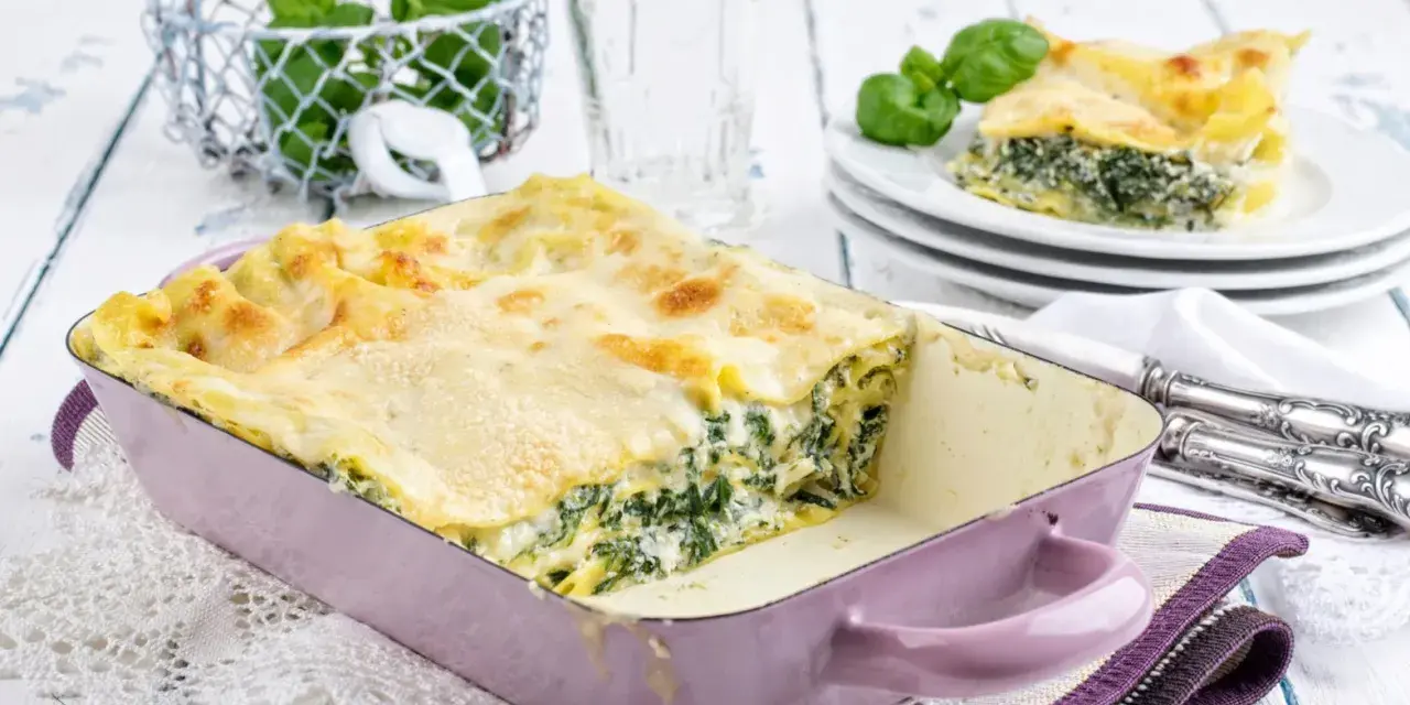 Herzhaftes Spinat-Lasagne-Rezept in einer lila Auflaufform, mit frischem Basilikum garniert.