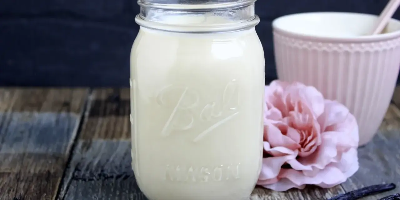 Selbstgemachter Kaffee-Sirup in einem Glas, mit Vanilleschoten und einer rosa Blume. Perfekt zum Kaffee creamer selber machen.
