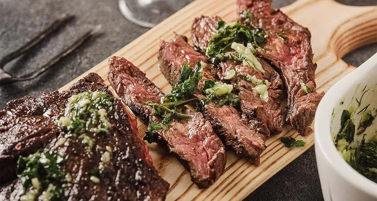 Saftiges, in Scheiben geschnittenes Flank Steak mit Kräutern und einer grünen Sauce auf einem Holzbrett serviert.