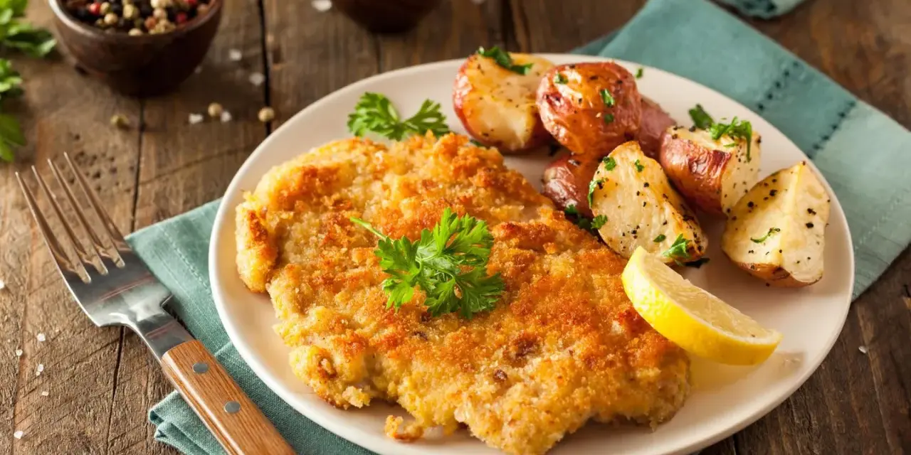 Goldbraunes Schnitzel, perfekt paniert, mit Rosmarinkartoffeln und Zitrone auf einem Teller. Ein Genuss, der zeigt, wie man ein Schnitzel paniert.