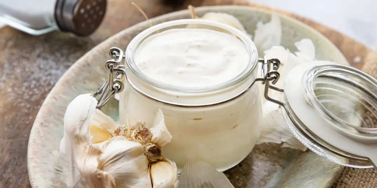 Frische Knoblauchsauce selber machen: cremige Sauce im Glas mit Knoblauchzehen und Salzstreuer im Hintergrund.