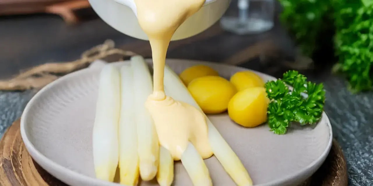 Sauce Hollandaise wird über weißen Spargel und Kartoffeln gegossen, um das Gericht zu verfeinern.
