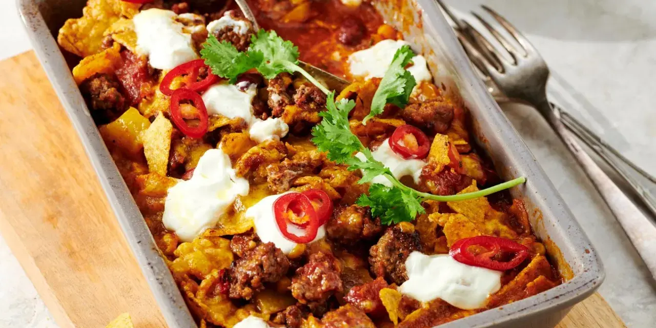 Herzhafter Shepherd's Pie mit Hackfleisch, Tortilla-Chips, Chili-Ringen und Klecksen saurer Sahne, garniert mit Koriander.