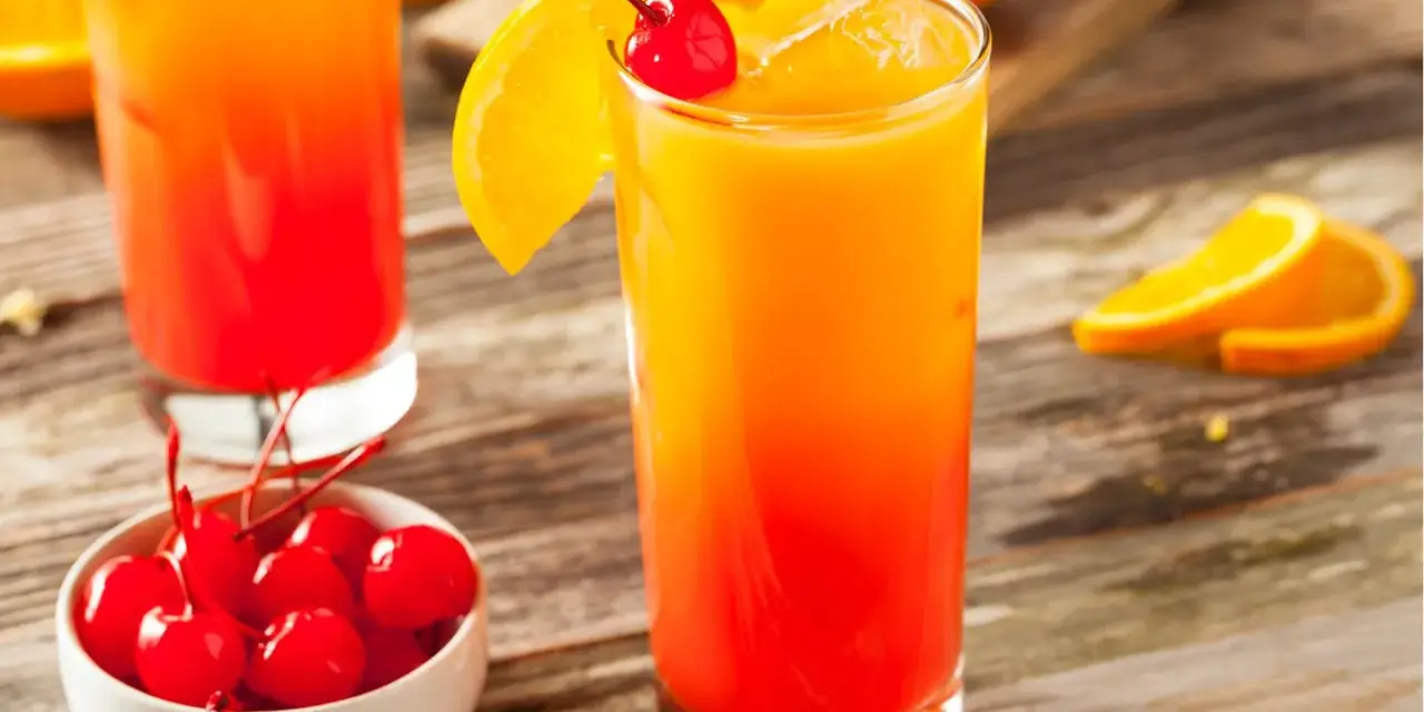 Ein erfrischender Tequila Sunrise mit Orangenscheibe und Kirsche, daneben eine Schale mit Kirschen.
