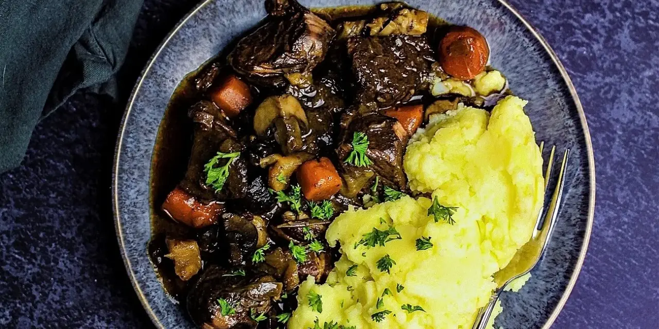 Herzhaftes Boeuf Bourguignon mit zartem Rindfleisch, Karotten und Pilzen, serviert mit cremigem Kartoffelpüree und Petersilie.