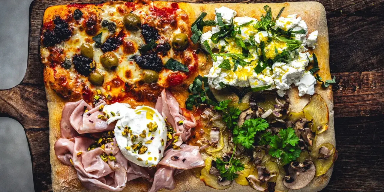 Vier verschiedene Beläge auf einer rechteckigen pizza al taglio: Oliven, Ricotta mit Kräutern, Mortadella mit Burrata und Kartoffeln mit Pilzen.