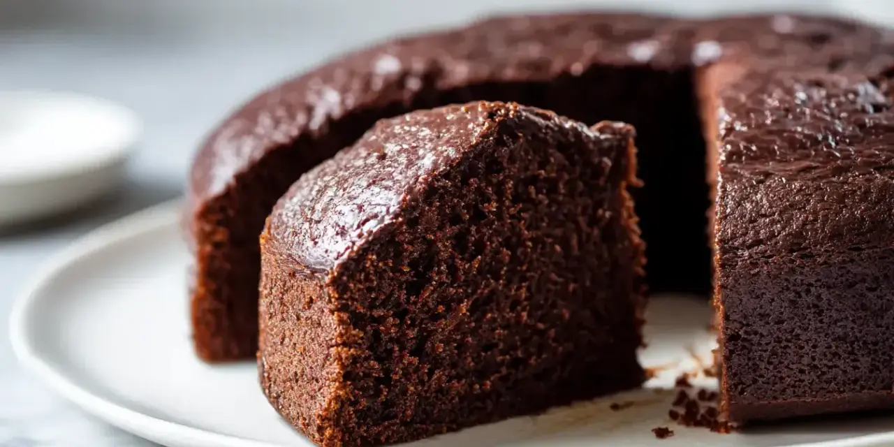 Saftiger Schokoladenkuchen, frisch aus dem Airfryer, auf einer weißen Platte. Ein Stück ist bereits angeschnitten.