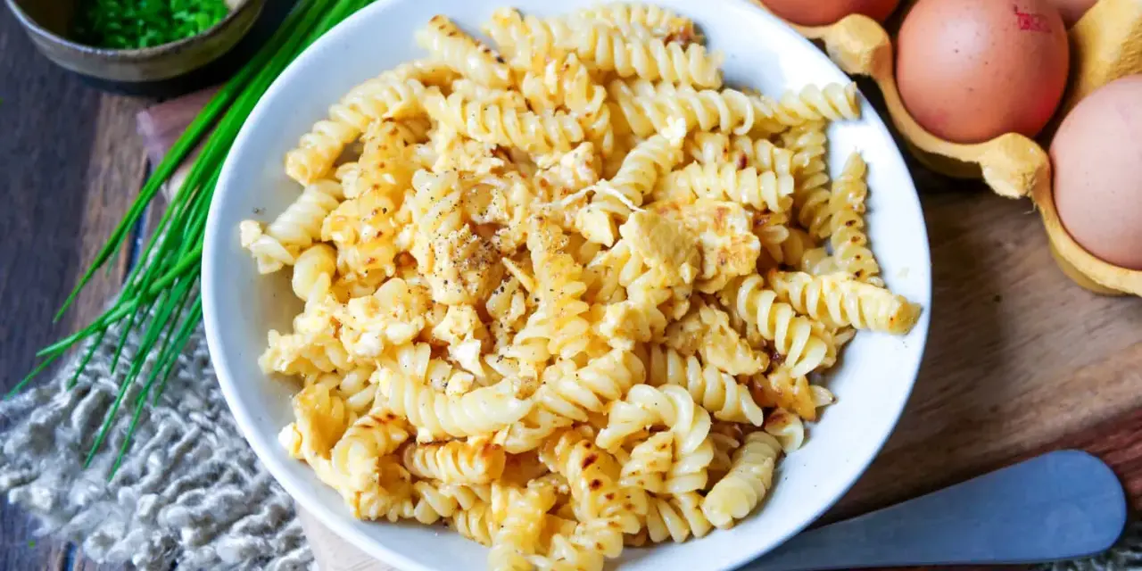 Fusilli-Nudeln mit Rührei, gewürzt mit Pfeffer. Daneben liegen frische Eier und Schnittlauch. Ein einfaches, aber leckeres Gericht: Nudeln mit Ei.