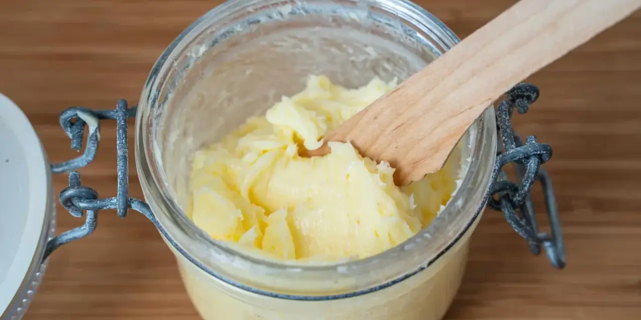 Frisch gemachte Butter in einem Glas, mit einem Holzspatel zum Butter selber machen.