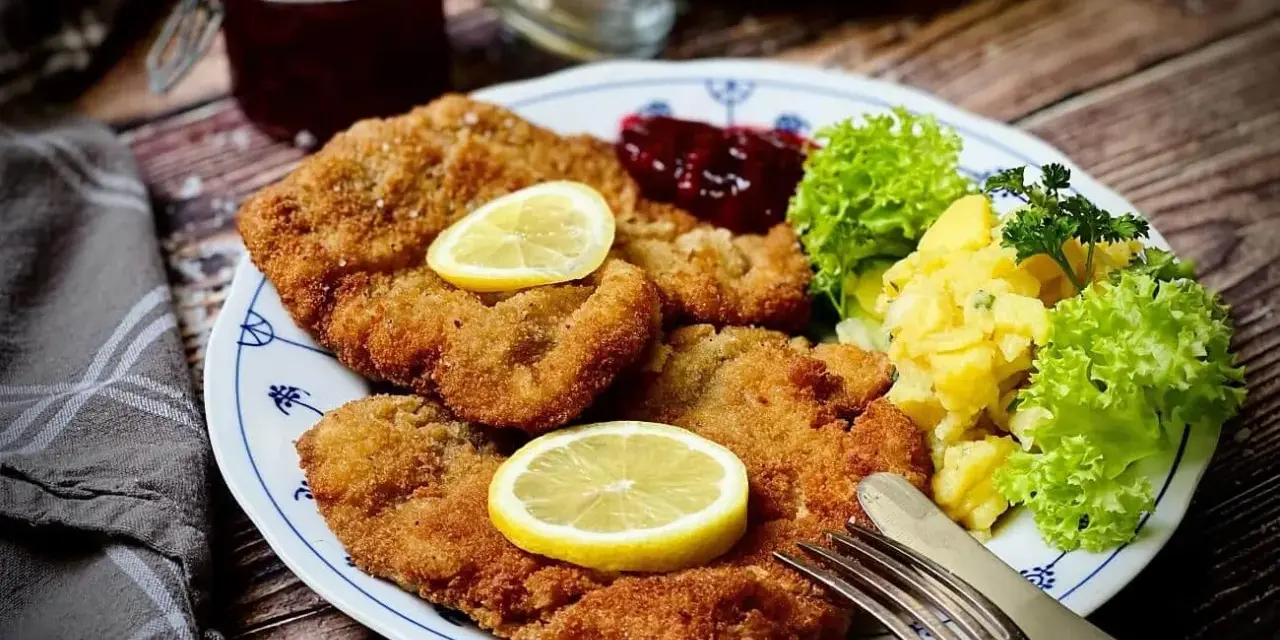 Ein köstlicher **Garnitur Wiener Schnitzel** mit Kartoffelsalat, Preiselbeeren und Zitrone auf einem Teller.