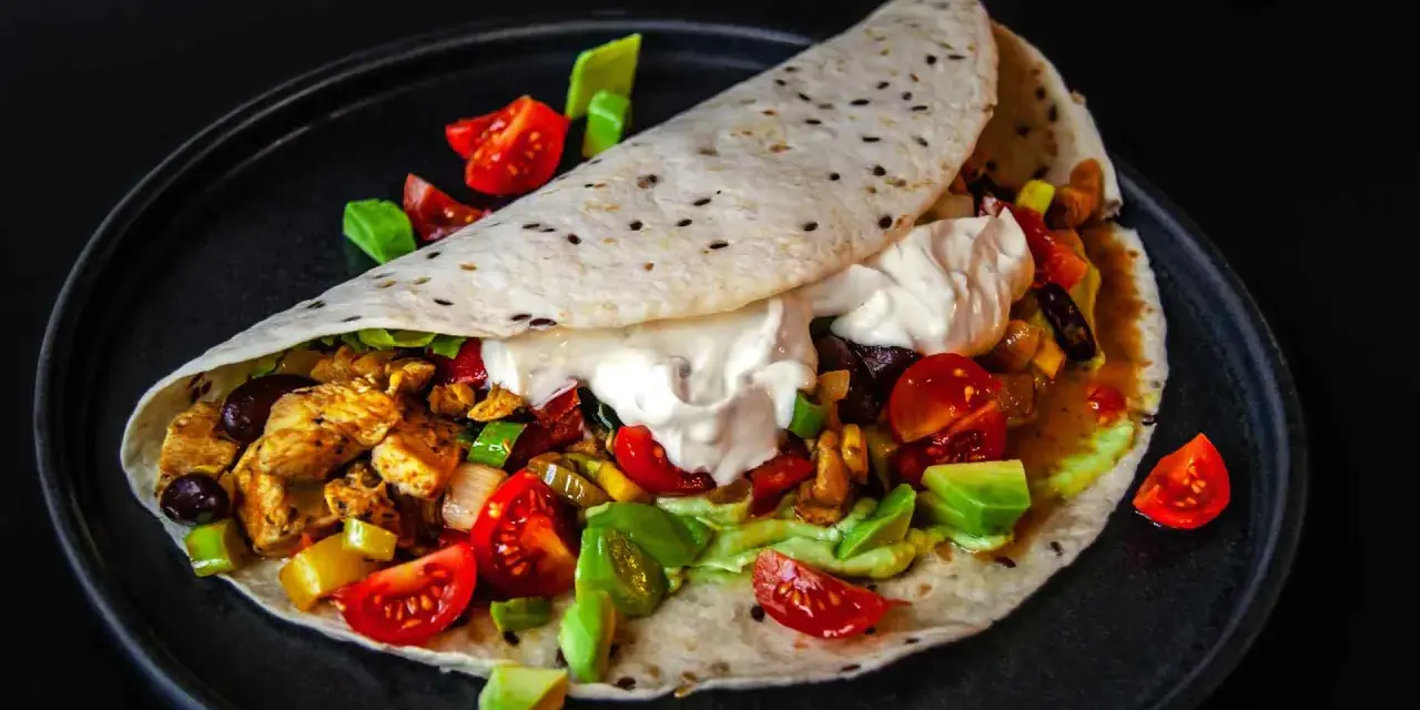 Saftige Fajitas de pollo mit Hähnchen, Gemüse, Avocado und einem Klecks Sauerrahm auf einem Tortilla-Wrap.