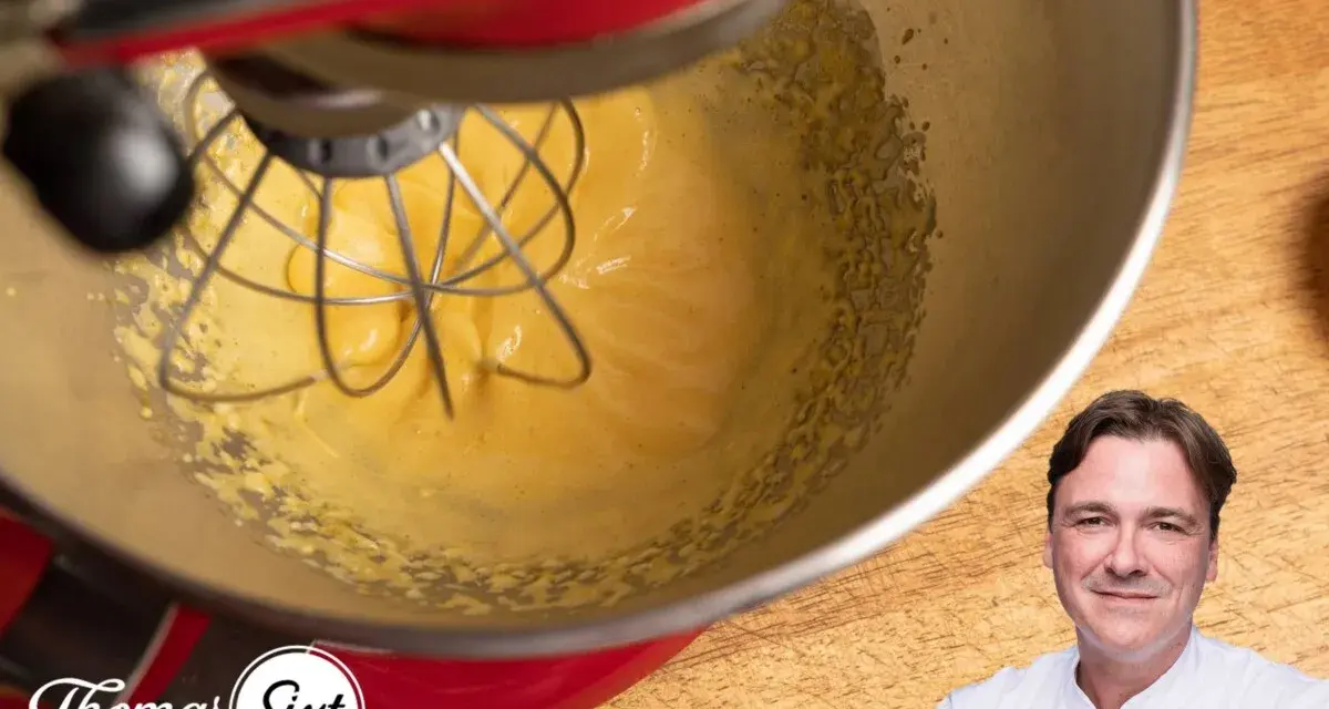 Küchenmaschine mixt eine cremige, gelbe Masse, die an Sauce Hollandaise erinnert. Ein Koch lächelt im Vordergrund.