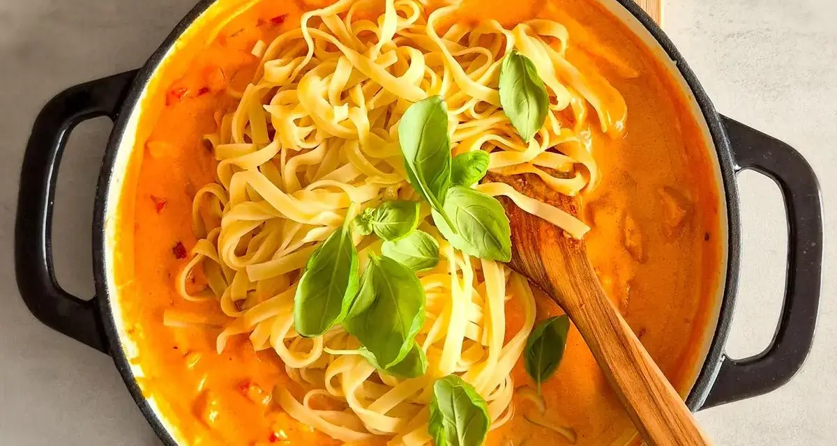 Cremiges Chicken Alfredo mit Tagliatelle, garniert mit frischem Basilikum, in einer schwarzen Pfanne.