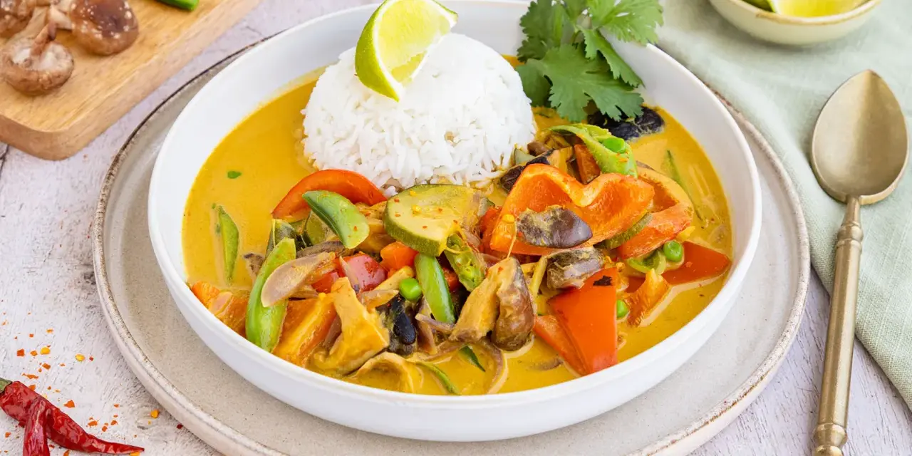 Ein bunter Thai Curry ohne Kokosmilch mit Reis, Paprika, Zucchini und Pilzen, garniert mit Limette und Koriander.