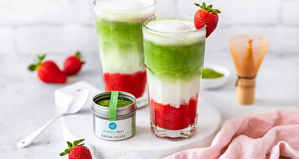Zwei geschichtete Erdbeer-Matcha-Latte-Getränke mit frischen Erdbeeren und Matcha-Pulver.