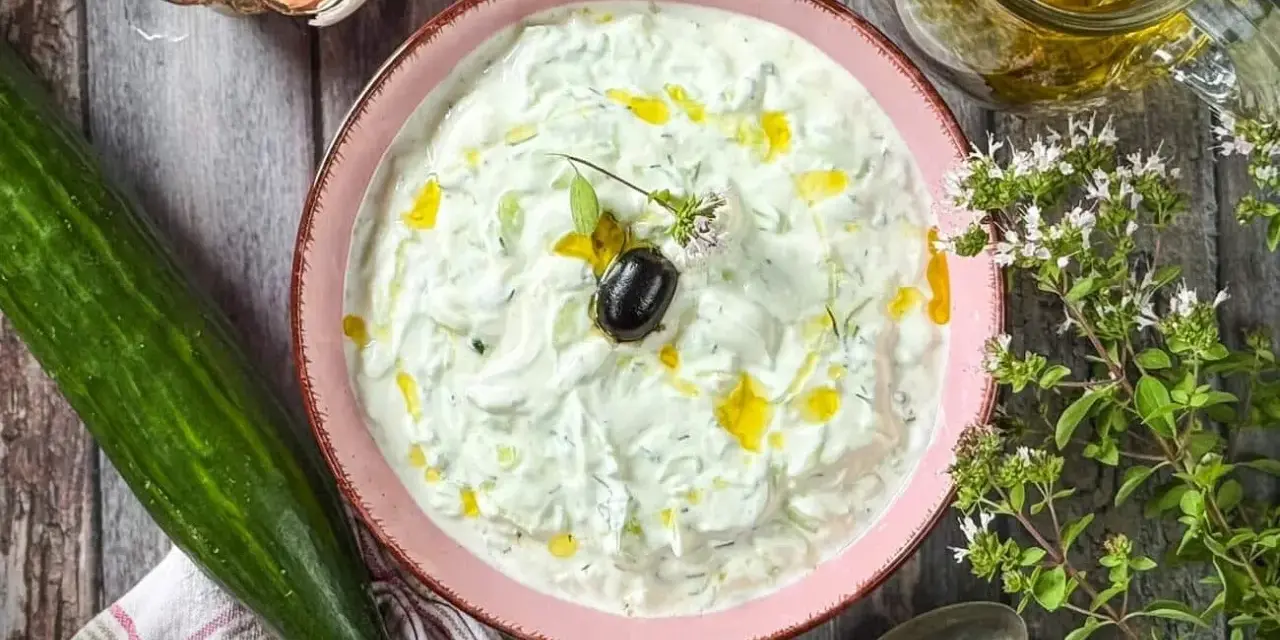 Frischer Tzatziki selbst machen: Cremiger Joghurt mit Gurke, Knoblauch, Dill und Olivenöl. Dazu eine Olive und Kräuter.