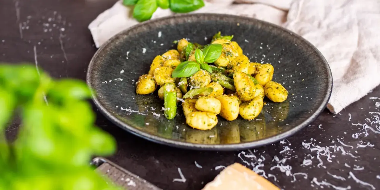 Gnocchi mit Spargel, garniert mit frischem Basilikum und Parmesan. Ein köstliches Gericht, das den Frühling auf den Teller bringt.