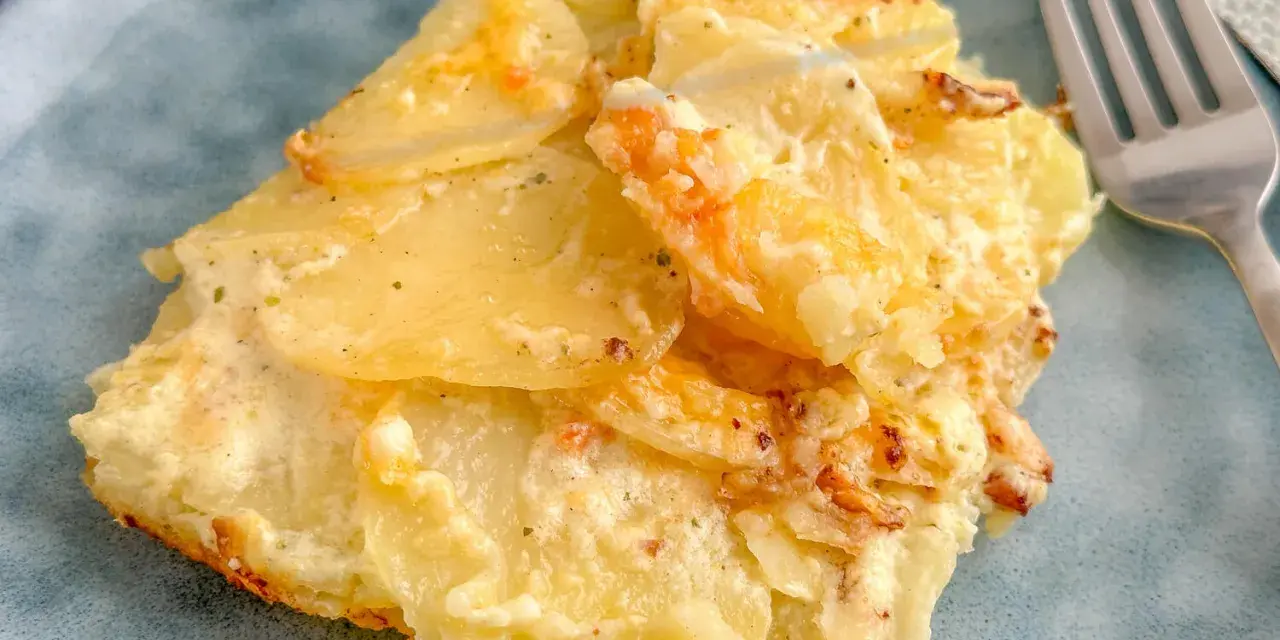 Ein Stück Kartoffelgratin einfach mit Sahne, goldbraun gebacken, auf einem blauen Teller. Daneben eine Gabel.
