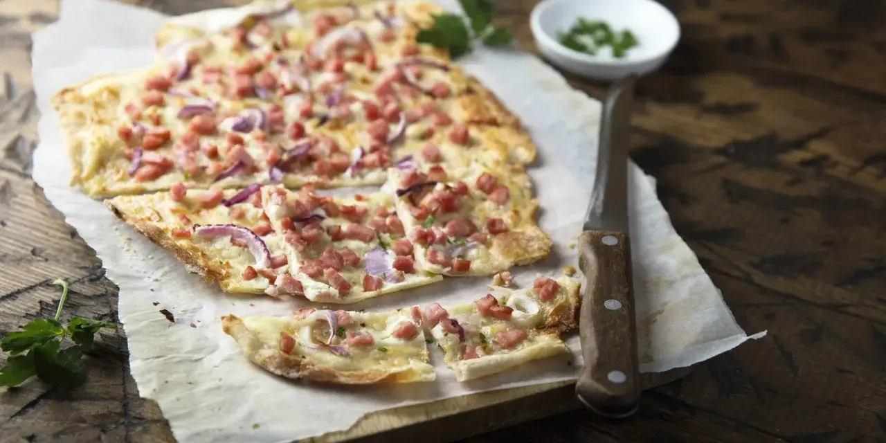 Flammkuchen mit Speck und Zwiebeln, eine klassische Idee für Flammkuchen Belag. Frisch und knusprig auf Holz serviert.