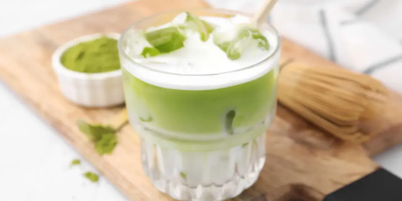 Erfrischender Matcha Latte mit Eis, Milch und einem Hauch von Starbucks-Rezept-Magie. Daneben eine Schale Matcha-Pulver und ein Chasen.
