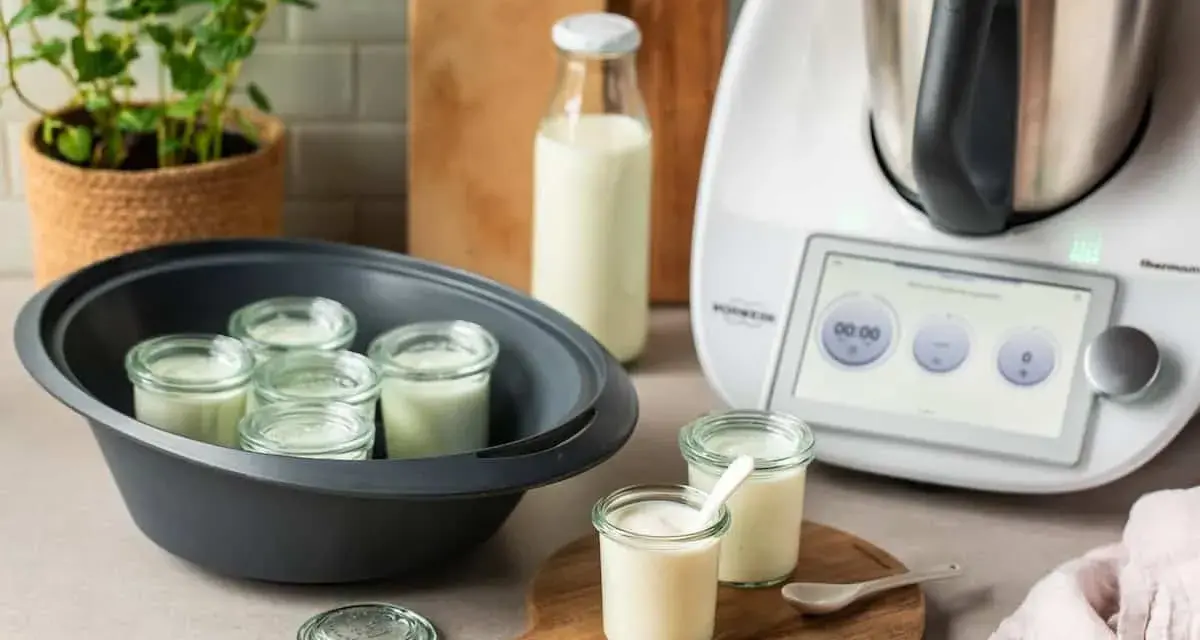 Kleine Gläser mit Joghurt in einem Dampfgarer, bereit, trinkjoghurt selber machen. Daneben ein Thermomix und Milchflasche.