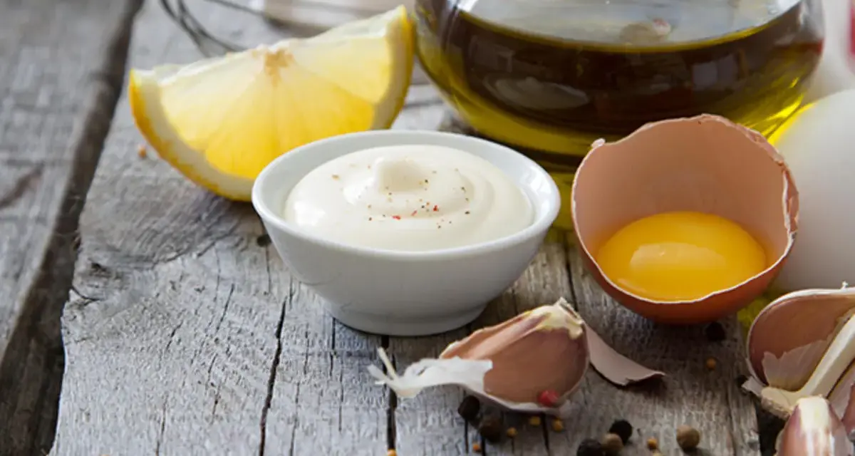Cremige Mayonnaise mit gekochtem Eigelb und Joghurt, garniert mit Pfeffer, neben Zitrone, Knoblauch und Olivenöl.