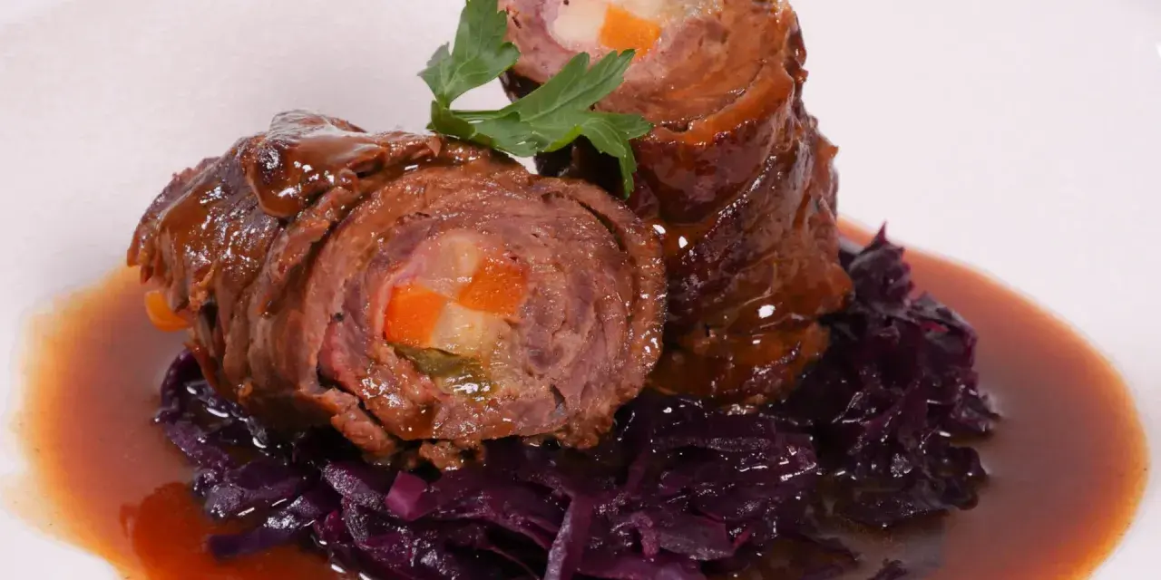 Zwei Rouladen mit Gemüsefüllung, serviert mit Rotkohl und Bratensoße. Köstliche Rouladen im Backofen zubereitet.