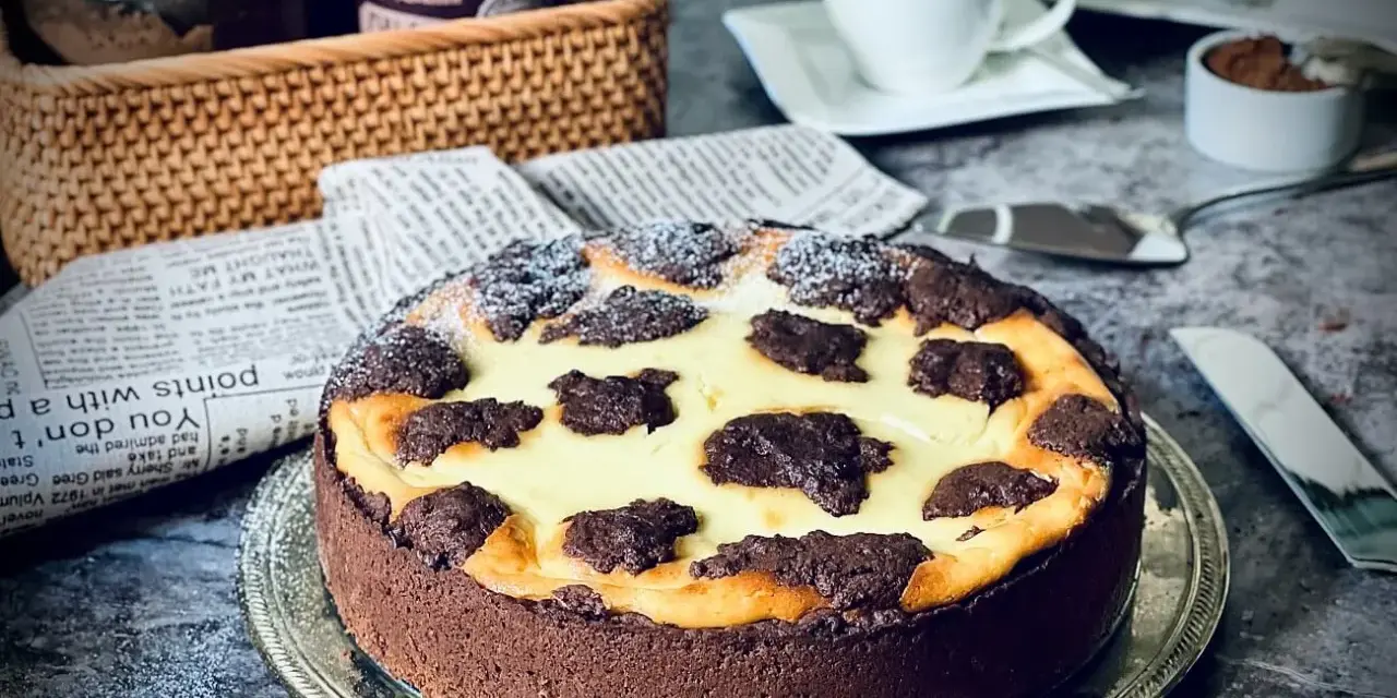 Ein köstlicher russischer Zupfkuchen mit Schokoladenboden und cremiger Füllung, bestäubt mit Puderzucker. Daneben eine Tasse Kaffee.