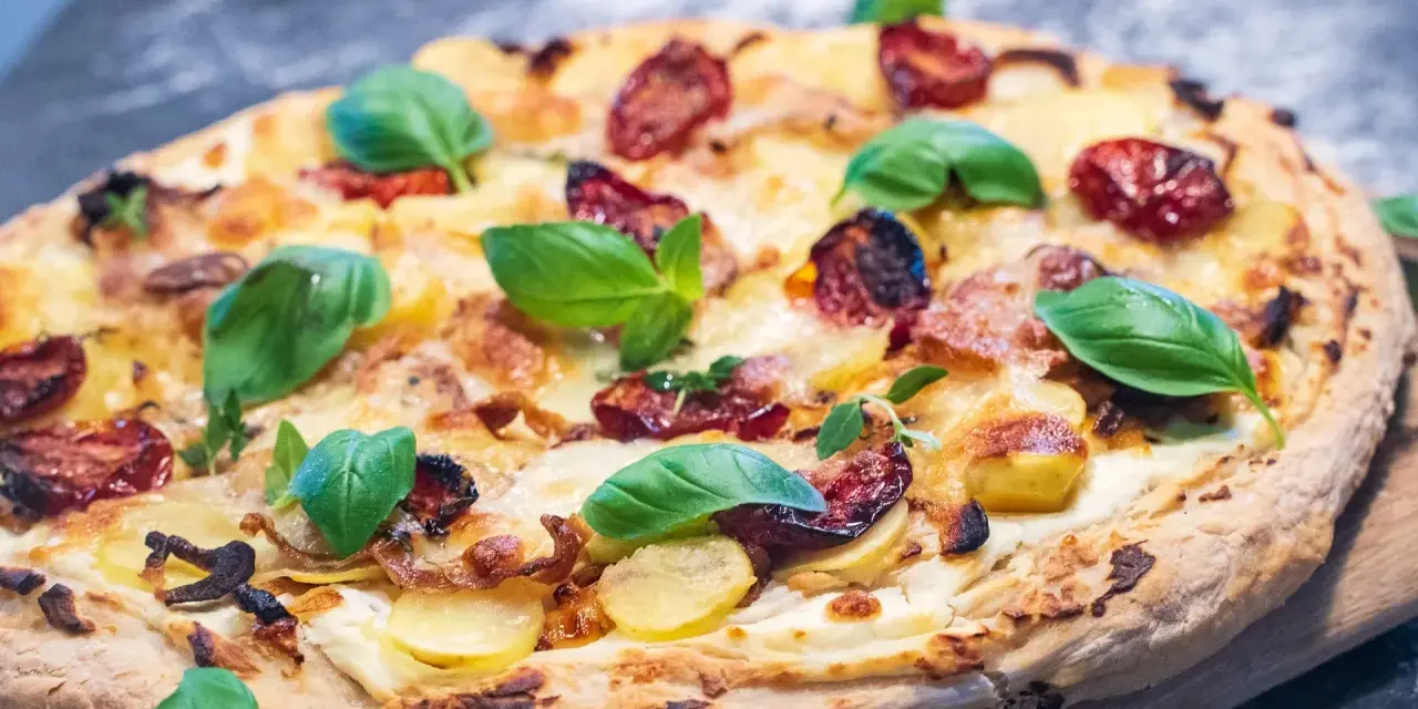 Eine köstliche Pizza Bianca mit Kartoffelscheiben, getrockneten Tomaten und frischem Basilikum.