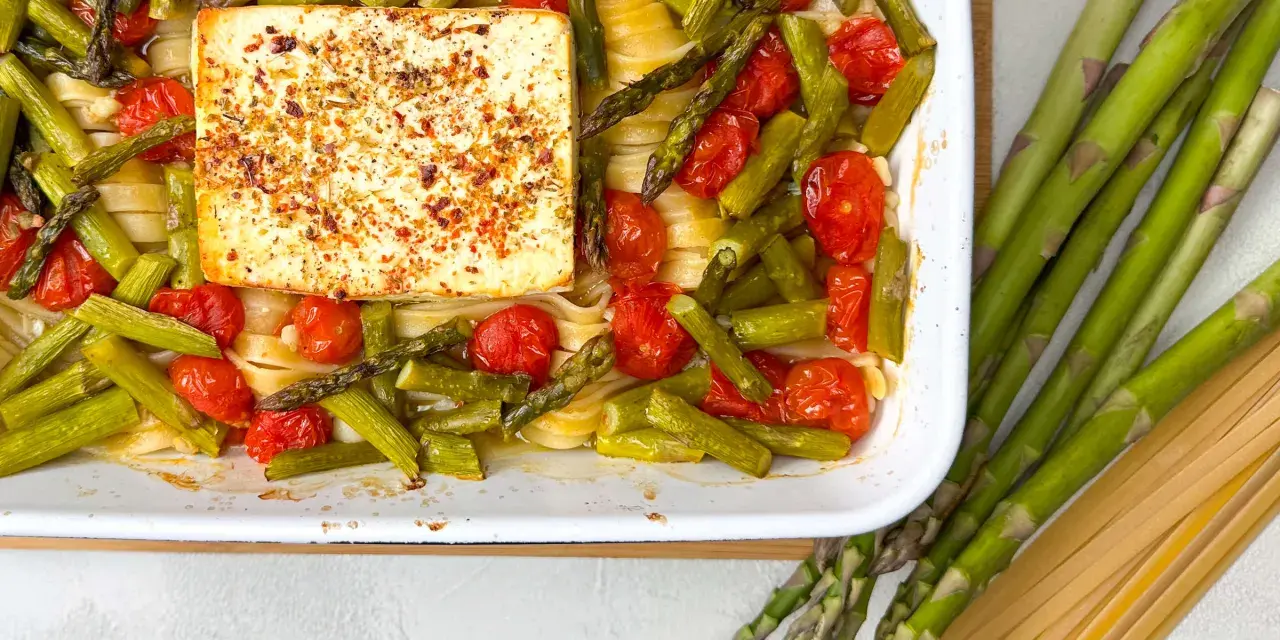 Spargel, Kirschtomaten und Pasta mit einem Block Feta, gewürzt mit Kräutern, in einer Auflaufform.