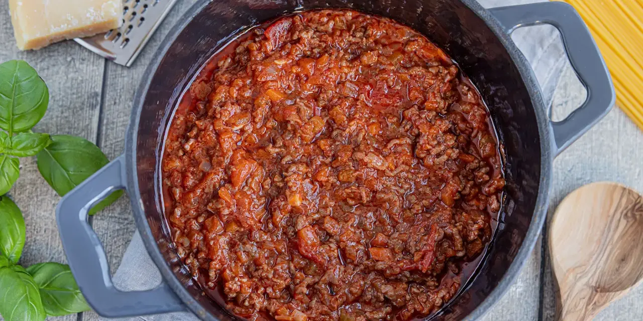 Herzhaftes Bolognese-Rezept original in einem Topf, mit frischem Basilikum, Parmesan und Spaghetti daneben.