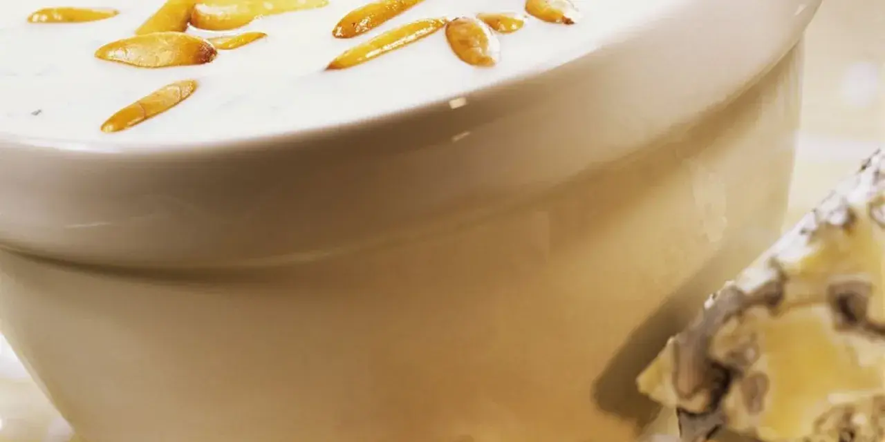 Cremige Gorgonzola-Sauce mit gerösteten Pinienkernen in einer Schüssel, daneben ein Stück Gorgonzola.
