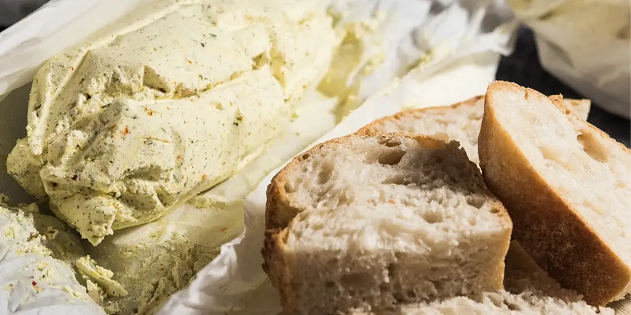 Ein Laib Kräuterbutter, wie Cafe de Paris Butter, liegt neben frisch geschnittenem Baguette.