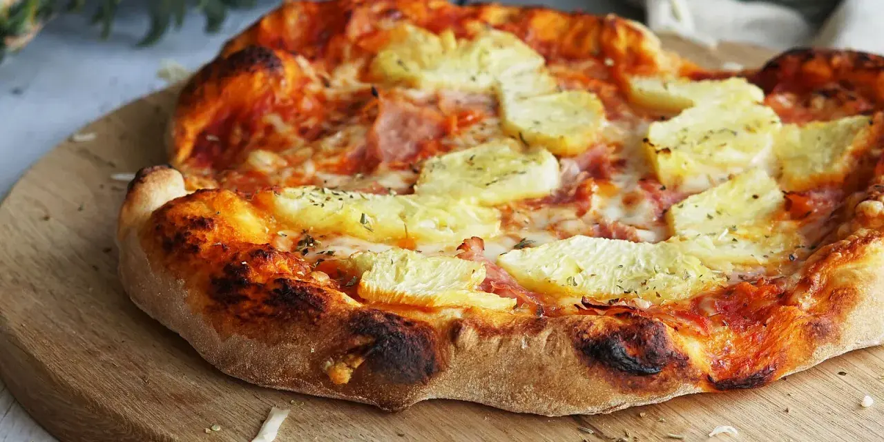 Eine köstliche Pizza Hawaii mit saftigen Ananasstücken und Schinken auf knusprigem Teig, garniert mit Kräutern.