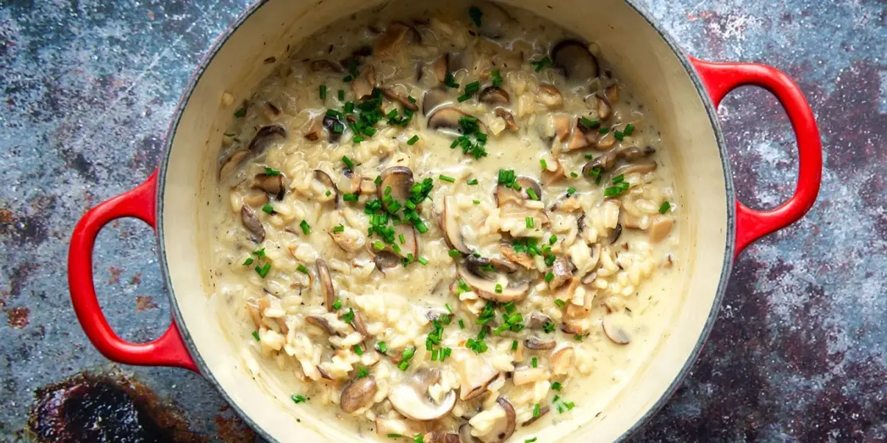Cremiges Pilzrisotto in rotem Topf, garniert mit Schnittlauch.