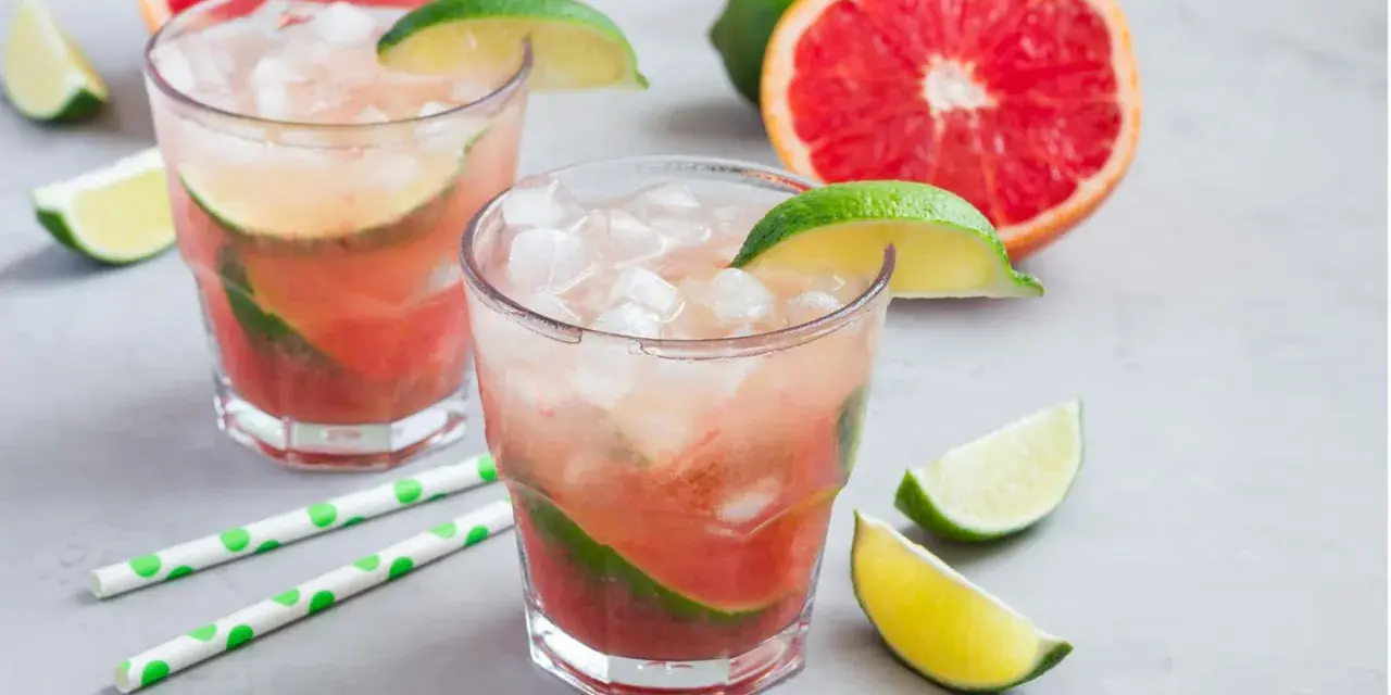 Erfrischender Aperol Paloma mit Grapefruit und Limette, serviert mit Eis und grünen Trinkhalmen.