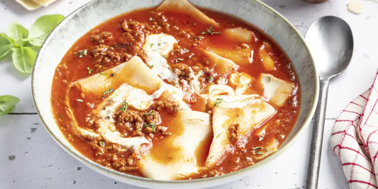 Herzhafte Lasagne Suppe in einer Schüssel, mit Hackfleischsauce, Nudelplatten und einem Klecks Sahne. Frisch garniert mit Basilikum.