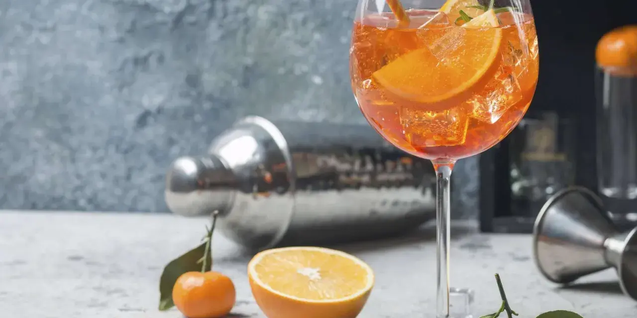 Erfrischender Aperol Spritz mit Orangenscheiben und Eiswürfeln, garniert mit Rosmarin. Ein Hauch von Sommer.