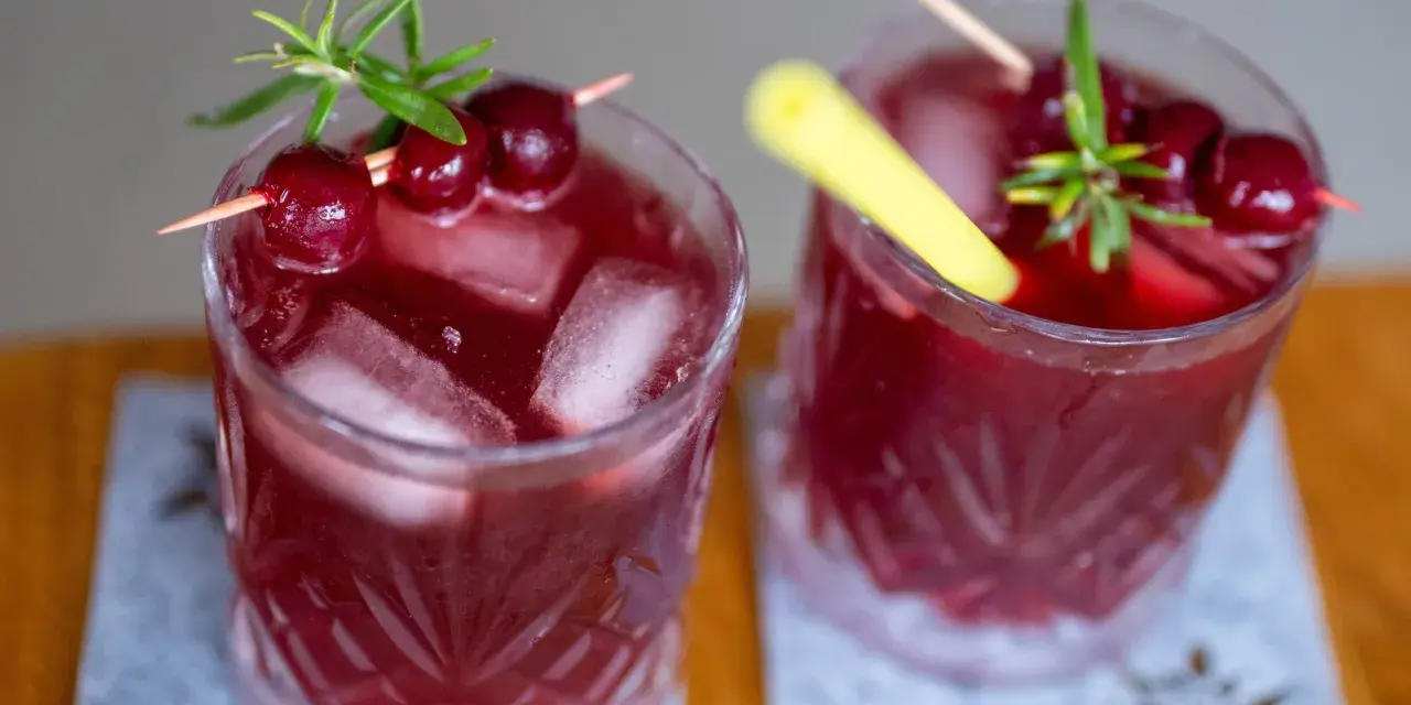 Zwei erfrischende, rote Mocktails mit Kirschen und Rosmarin, perfekt für einen entspannten Abend.
