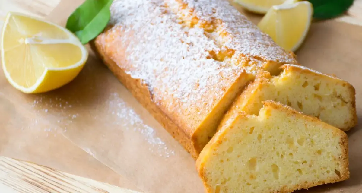 Saftiger veganer Zitronenkuchen, bestäubt mit Puderzucker, mit frischen Zitronenspalten und Blättern garniert.