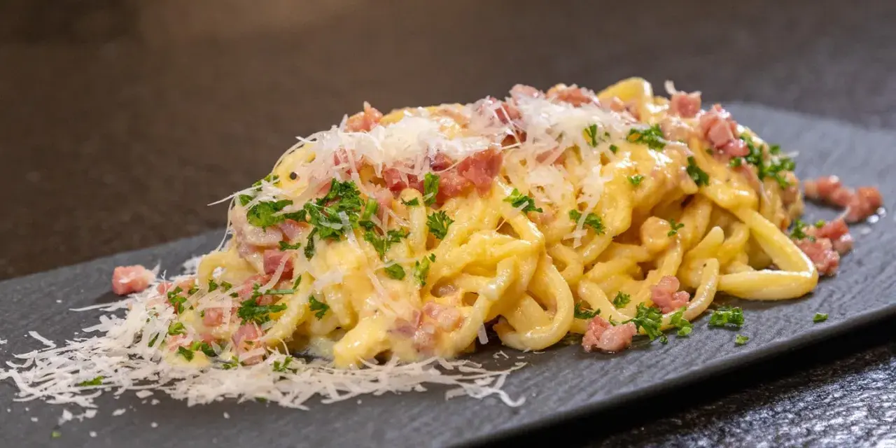 Ein Teller cremiger Spaghetti Carbonara, garniert mit Speckwürfeln, Petersilie und frisch geriebenem Parmesan.