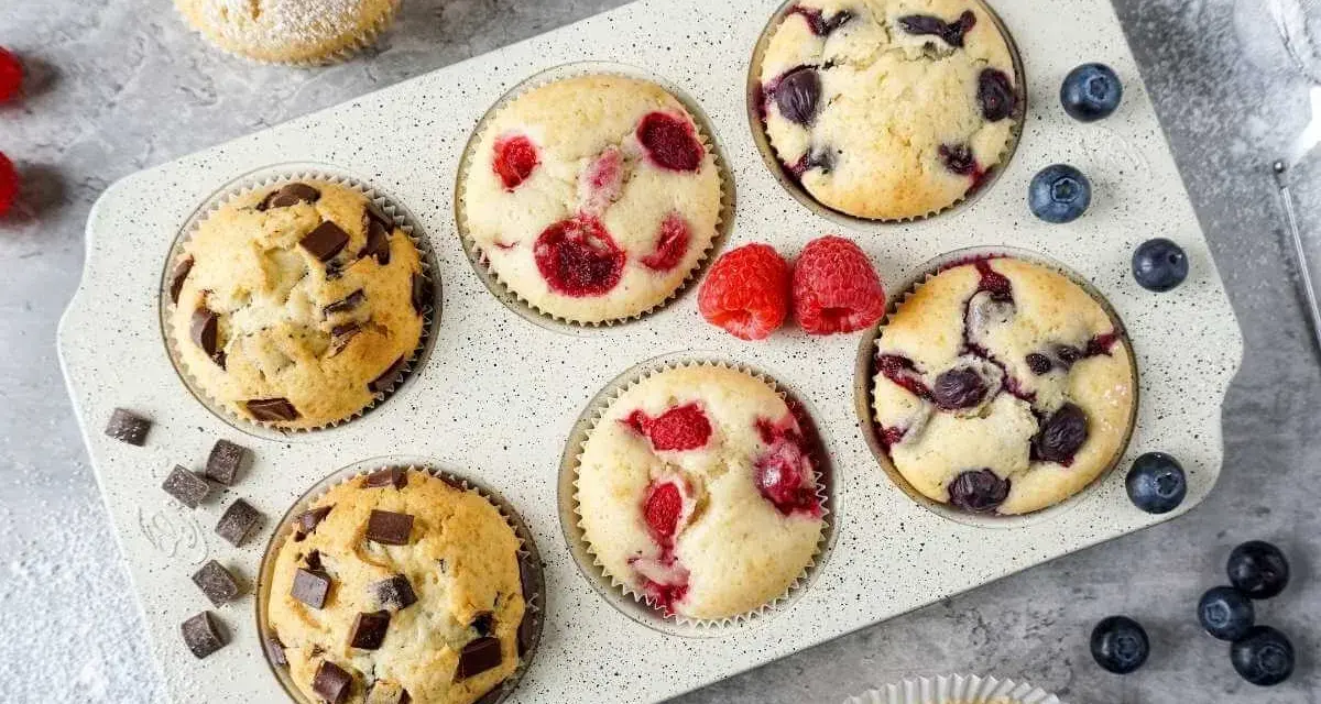 Leckeres Muffins Rezept: Schoko-, Himbeer- und Blaubeermuffins in einer Form, daneben frische Beeren und Schokostückchen.