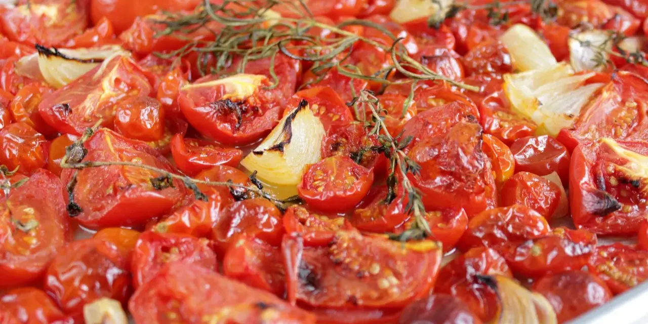 Tomatensauce aus dem Ofen: Geröstete Tomaten und Zwiebeln mit Rosmarin, die köstlich duften und bereit sind, zu einer aromatischen Sauce verarbeitet zu werden.