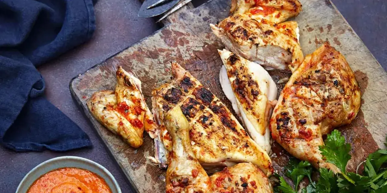 Saftiges Peri Peri Chicken, gegrillt und mit einer würzigen Sauce serviert, liegt auf einem Holzbrett.