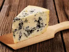 Ein Stück Blauschimmelkäse, perfekt für eine cremige blue cheese sauce, liegt auf einem Holzbrett.