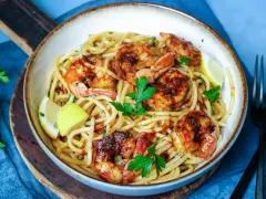 Ein Teller mit köstlichen Spaghetti mit Garnelen, garniert mit frischer Petersilie und Zitronenspalten.