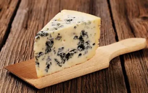 Ein Stück Blauschimmelkäse, perfekt für eine cremige blue cheese sauce, liegt auf einem Holzbrett.