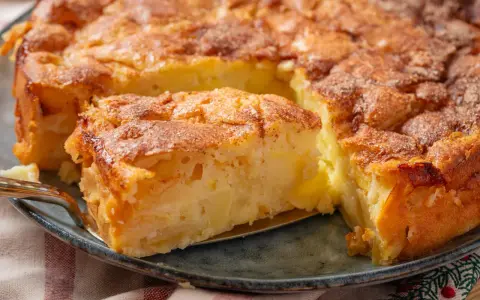 Ein saftiger apfelkuchen mit schale, goldbraun gebacken und mit Zimt bestreut. Ein Stück wird gerade herausgehoben.