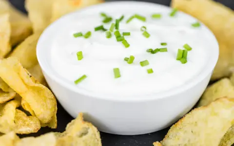 Schüssel mit cremiger Sour Cream, garniert mit Schnittlauch, umgeben von knusprigen Kartoffelchips.